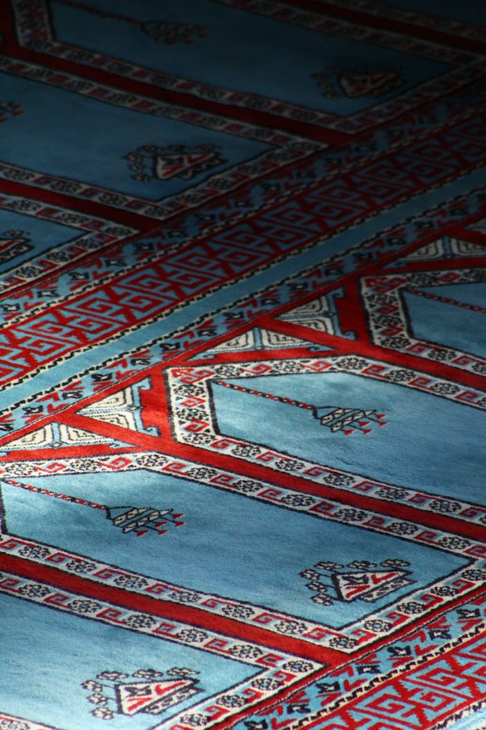 Close-up view of a beautifully decorated blue and red carpet in a mosque setting.
