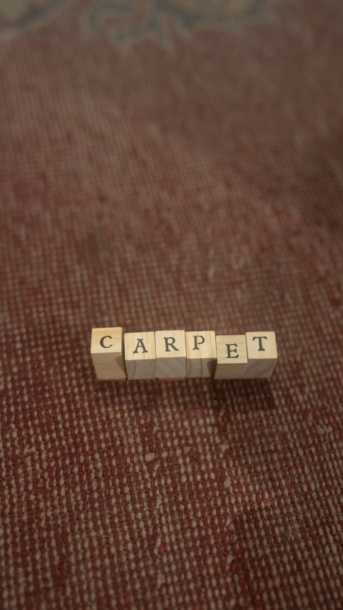 Wooden blocks spelling the word 'carpet' on a textured surface.