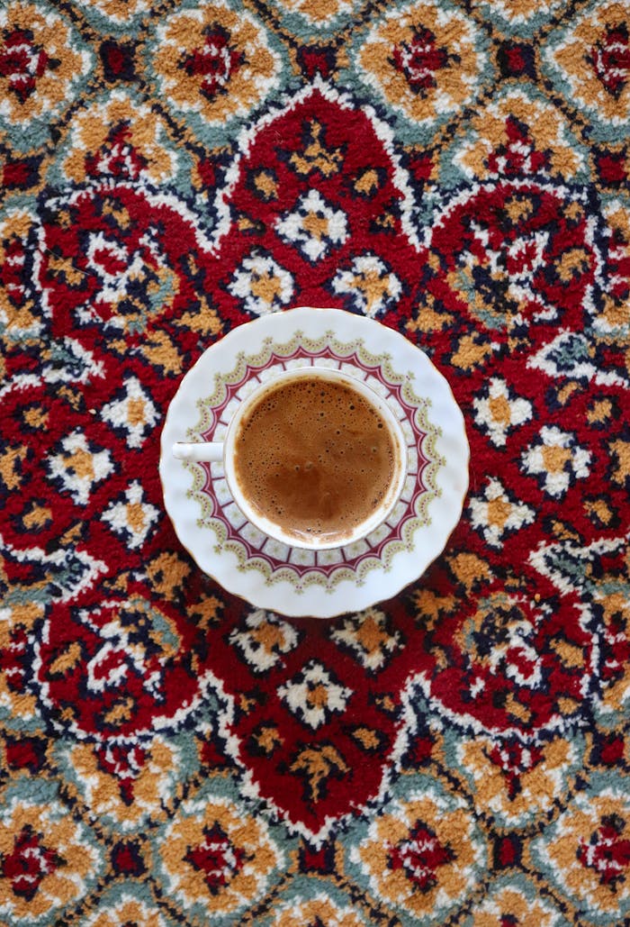 Top view of a cup of coffee placed on an intricately designed Persian carpet, showcasing cultural elegance.